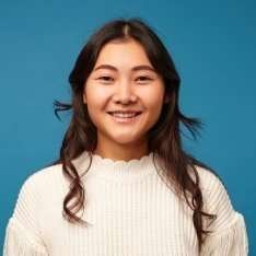 Smiling woman in a cream knit sweater against a blue background